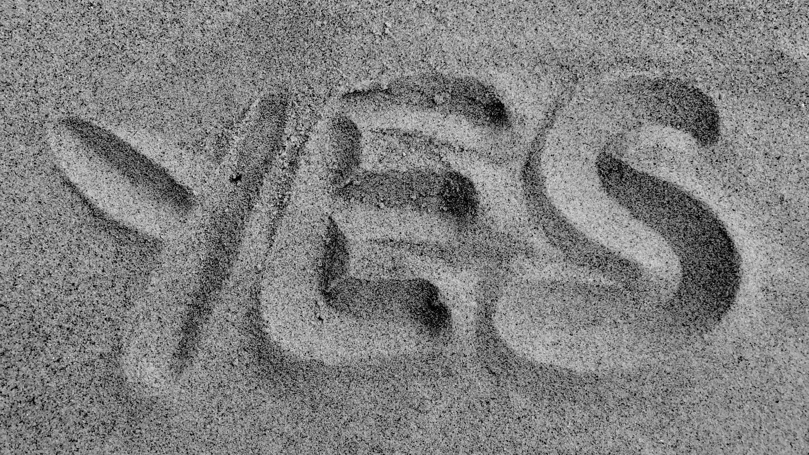 Black and white image of the word 'yes' drawn in sand