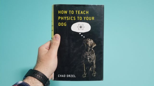 A hand holding the book How to teach physics to your dog by Chad Orzel