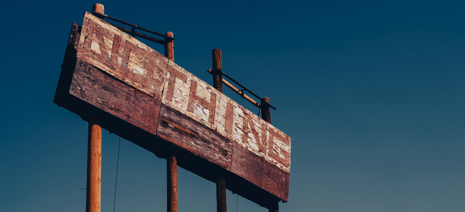 An faded wooden sign that says the word &quot;Nothing&quot; in large blocky letters, set against a clear blue sky. Photo by Evan Buchholz on Unsplash.com